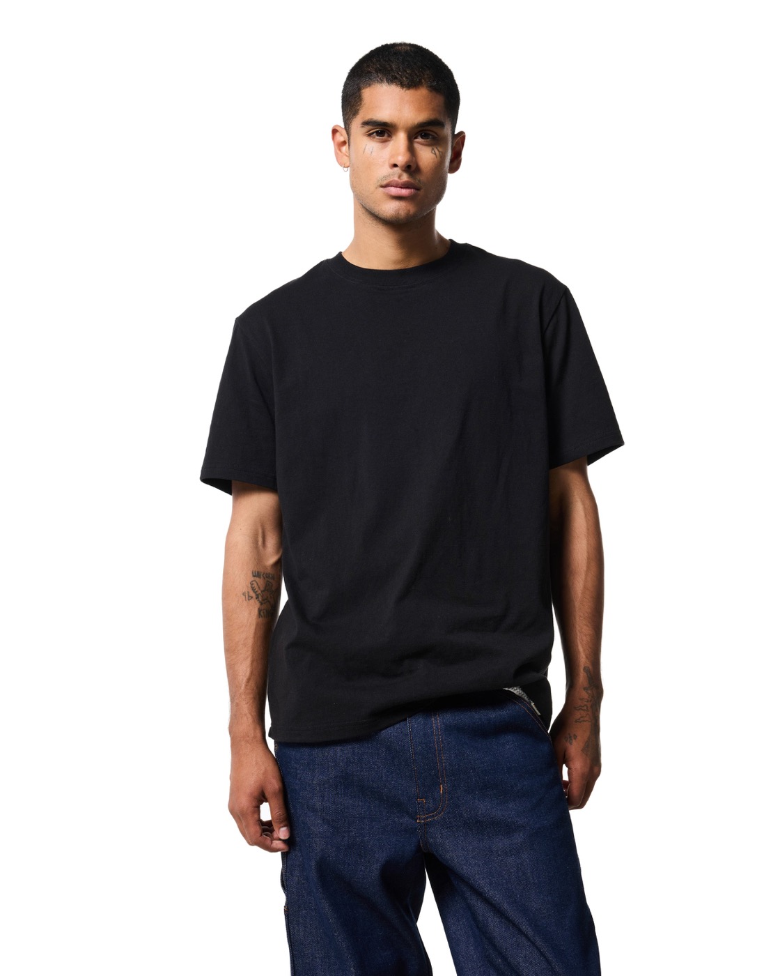 A man in the Classic tee in jet black and dark denim jeans, from the front against white