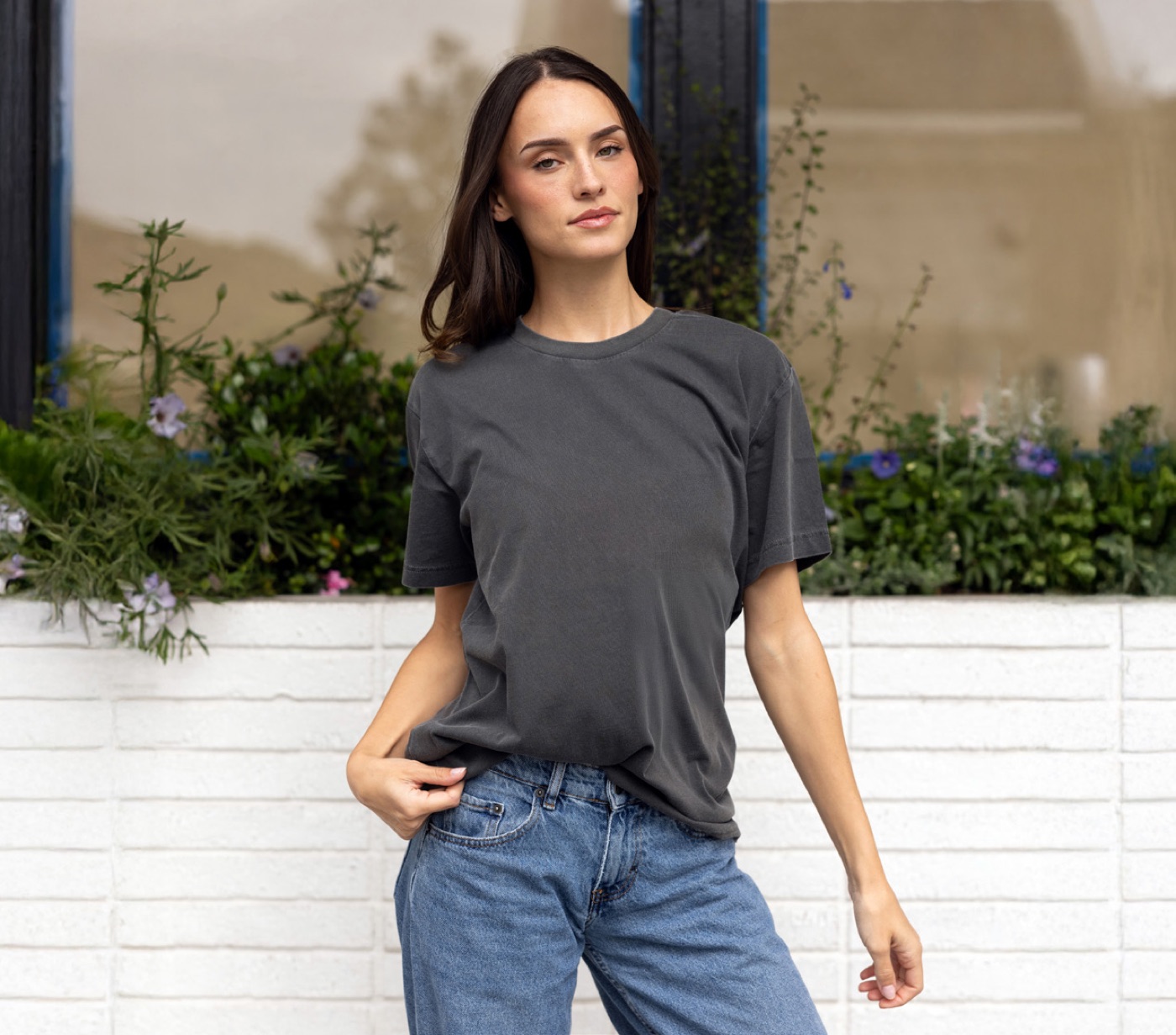 A woman in the PRM180PT tee in pigment black, standing by a white brick planter