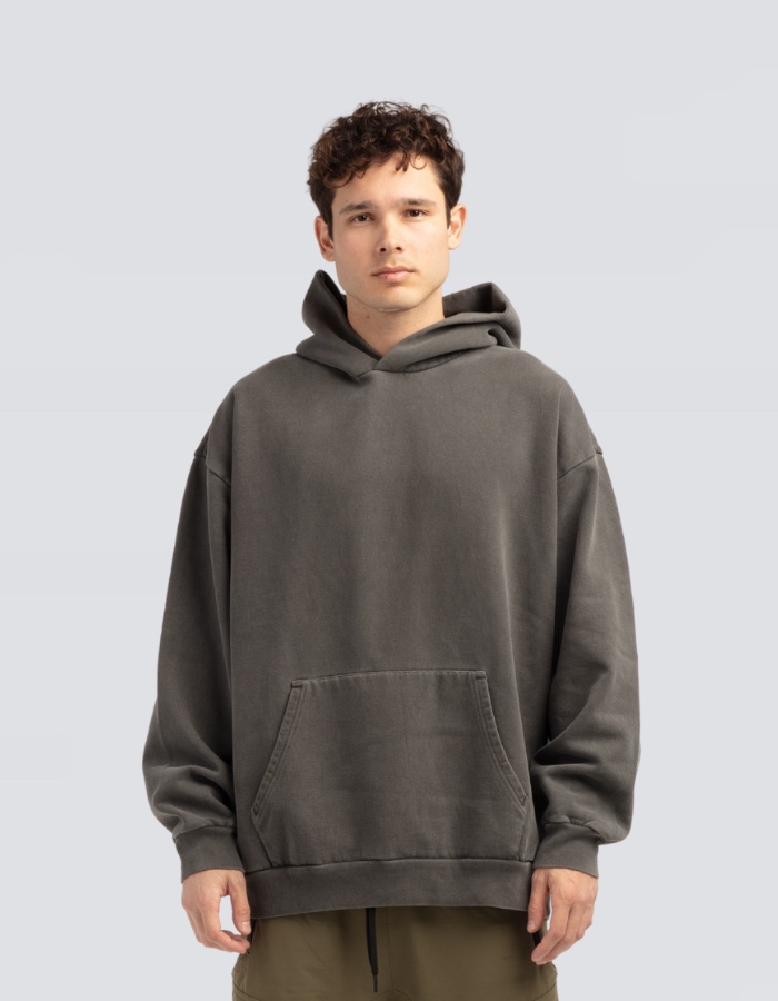 A man in the Elevated hoodie in pigment black, a washed charcoal grey, front view on a plain grey ground